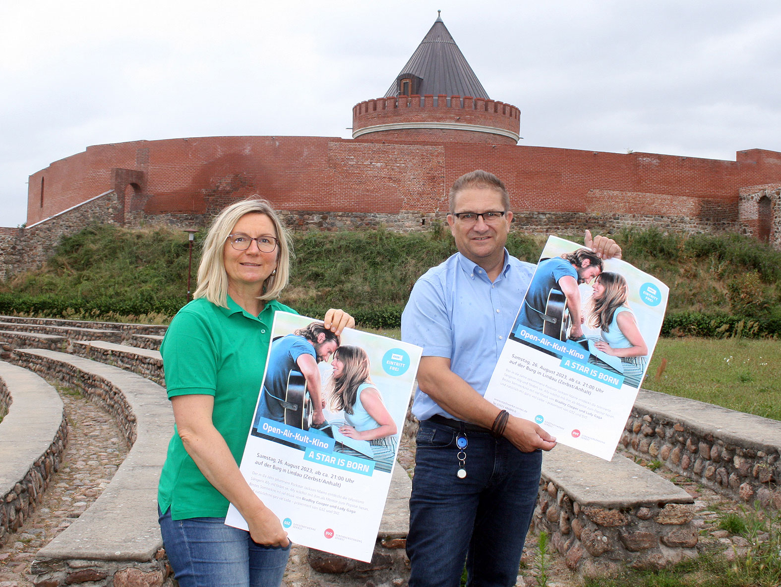 Jana Eisfeld vom Heimat- und Verkehrsverein Lindau und Frank Sieweck von der EMS präsentieren am Fuße der Burg die aktuellen Plakate zum diesjährigen Open-Air-Kult-Kino. Foto EMS